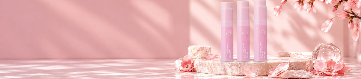 Three Ellumie PDRN Collagen Multi Balm sticks on a pink marble podium with cherry blossoms and a glass sphere